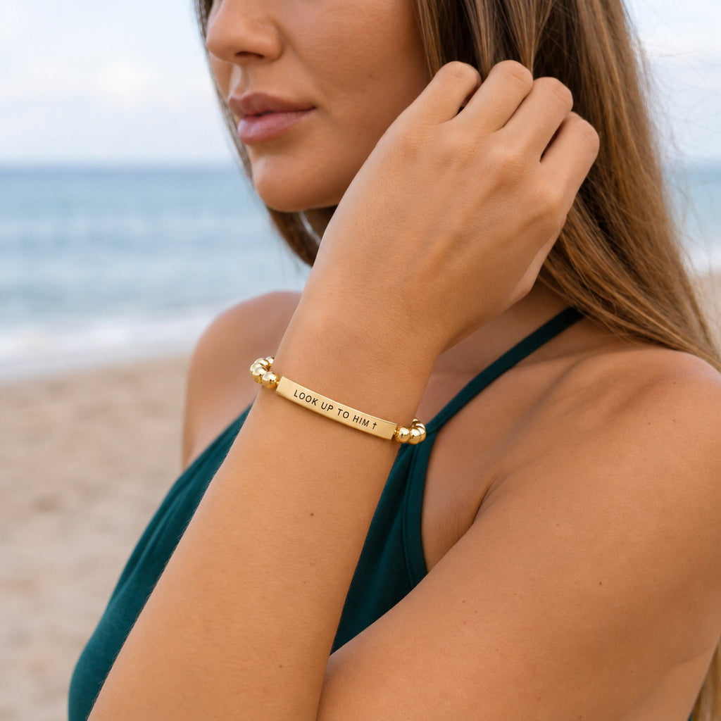 Woman at the beach wearing the Gold Look Up to Him bracelet